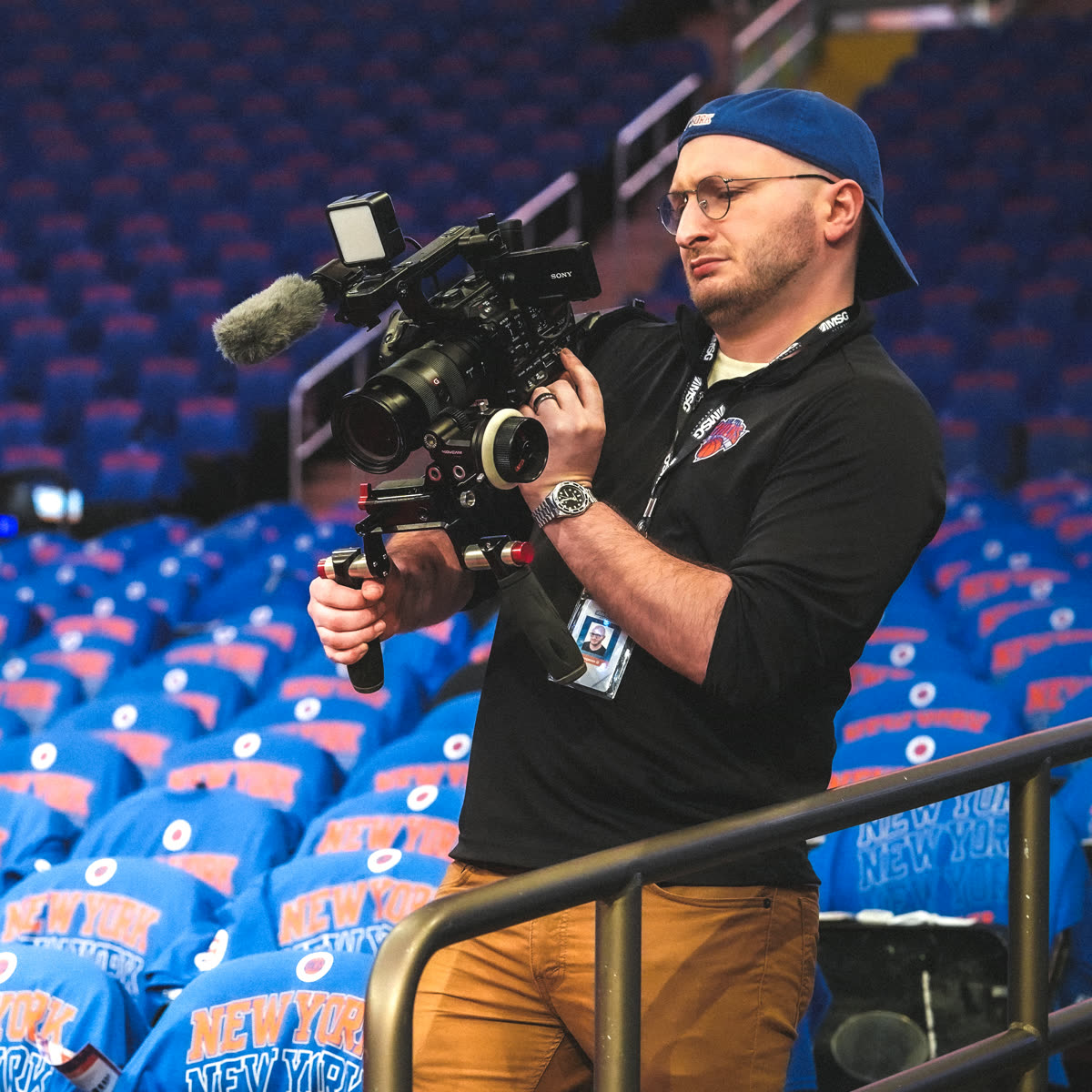 Ben Golden shouldering a camera rig in an empty Madison Square Garden, every seat draped with a blue New York playoff shirt