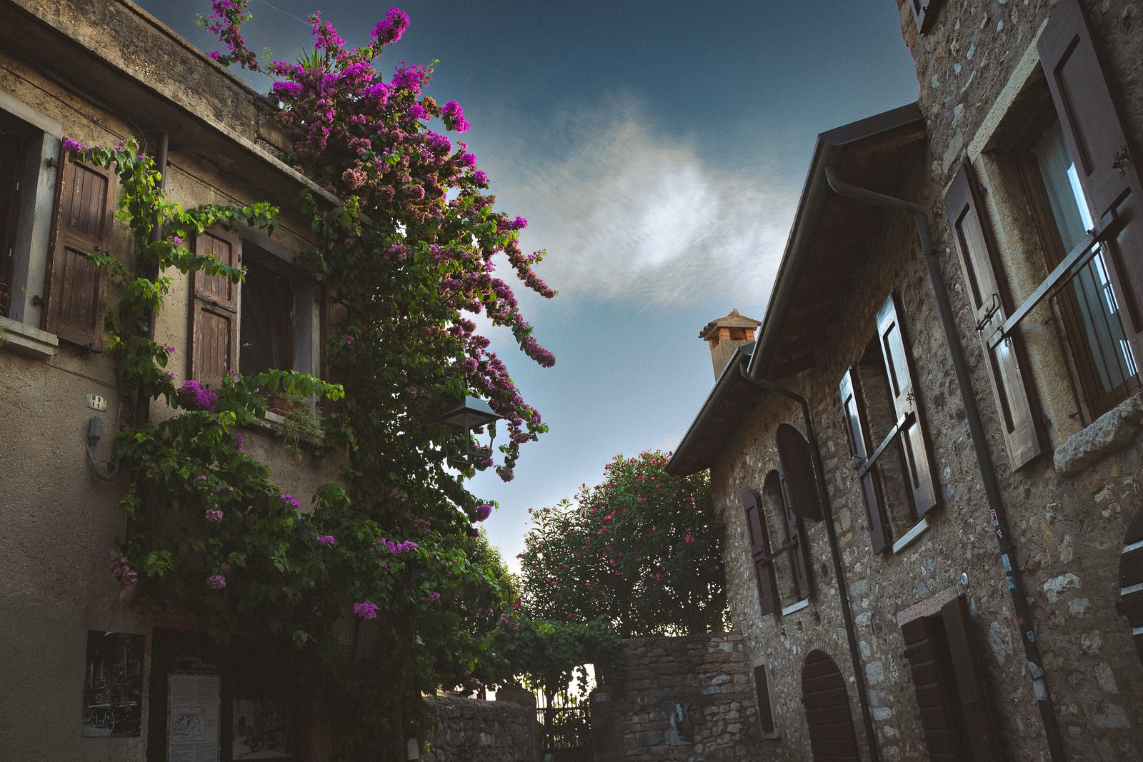 A narrow stone alley in Malcesine, bougainvillea spilling over shuttered windows under a deep blue sky.