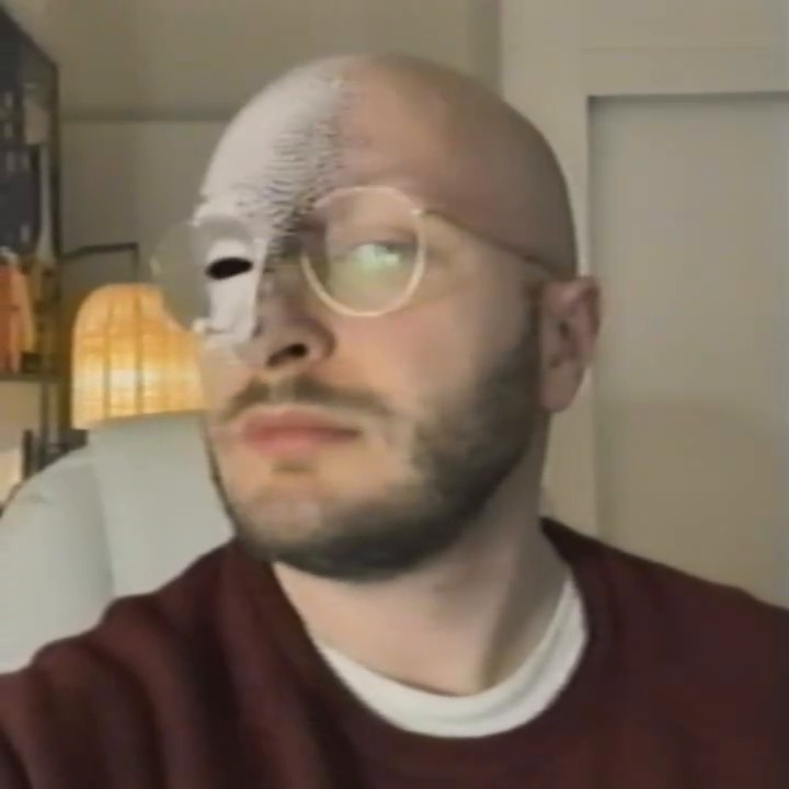 Both eyes are now slots behind his glasses, one lens catching the light.